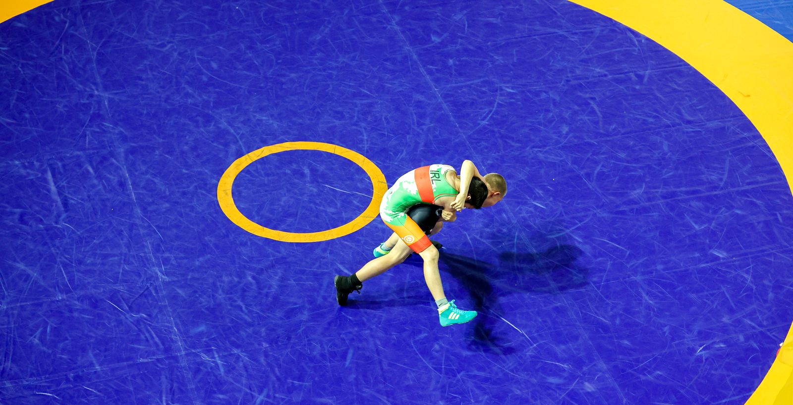 A young wrestler in an Ireland singlet works for position on the blue competition mat at the Irish Open
