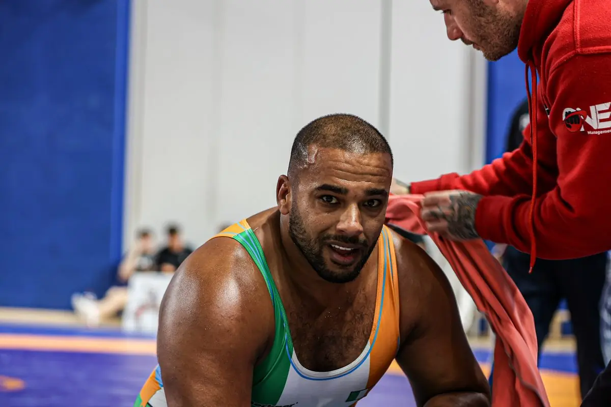 An Ireland wrestler in a tricolour singlet takes a break matside with his coach at the Irish Open